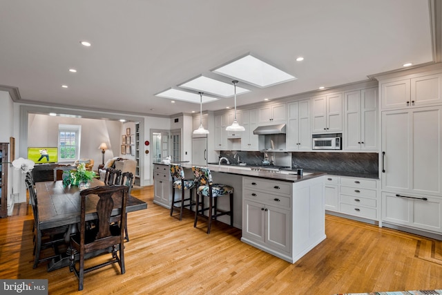 kitchen featuring light hardwood / wood-style flooring, hanging light fixtures, stainless steel microwave, and a skylight