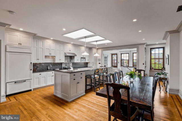 kitchen featuring light hardwood / wood-style floors, a skylight, a center island with sink, and hanging light fixtures