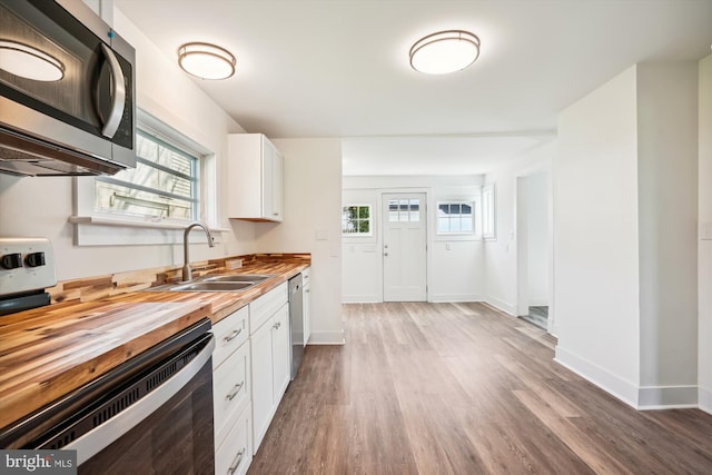 kitchen featuring wooden counters, appliances with stainless steel finishes, sink, wood-type flooring, and white cabinets