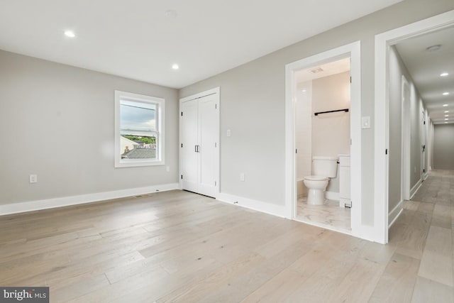 unfurnished bedroom featuring a closet, light wood-type flooring, and ensuite bath