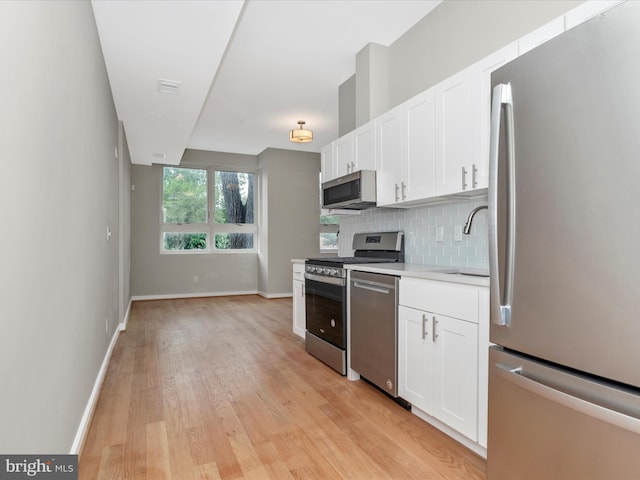 kitchen featuring appliances with stainless steel finishes, light wood-type flooring, backsplash, sink, and white cabinets