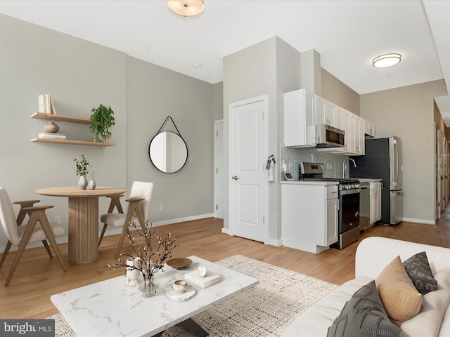 kitchen featuring backsplash, white cabinetry, light hardwood / wood-style flooring, and appliances with stainless steel finishes