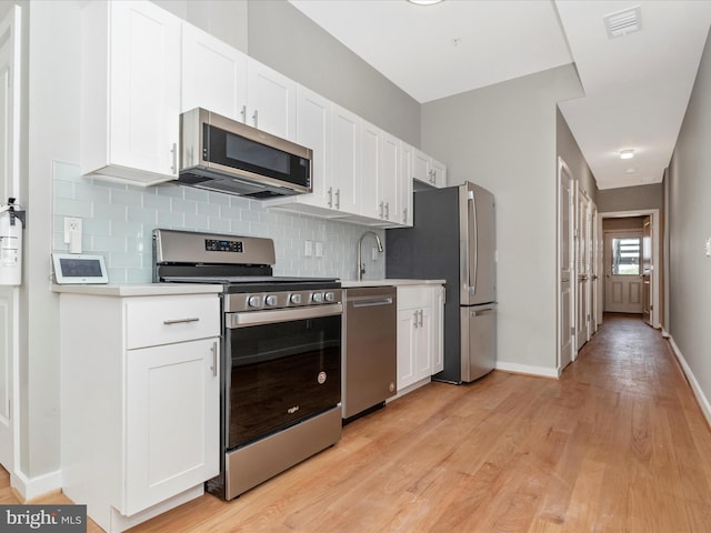 kitchen with backsplash, white cabinets, sink, light wood-type flooring, and stainless steel appliances