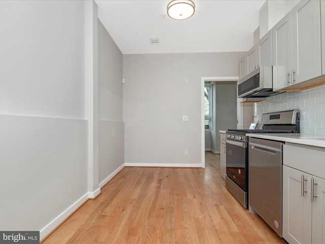 kitchen with decorative backsplash, gray cabinets, light wood-type flooring, and appliances with stainless steel finishes