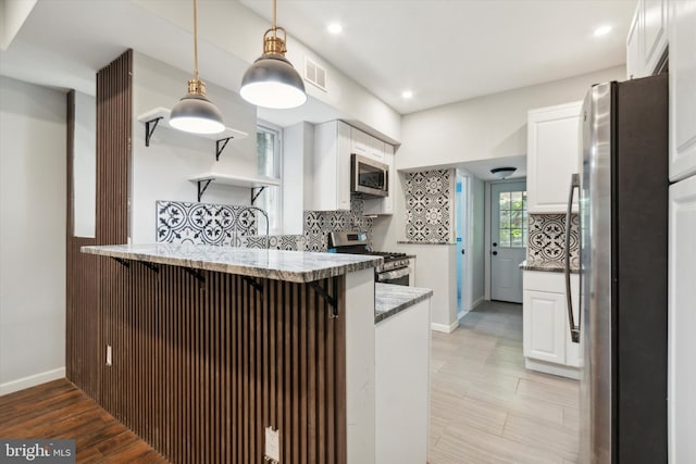 kitchen with white cabinetry, kitchen peninsula, appliances with stainless steel finishes, and tasteful backsplash