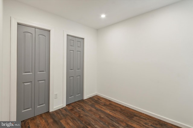 unfurnished bedroom featuring two closets and dark wood-type flooring