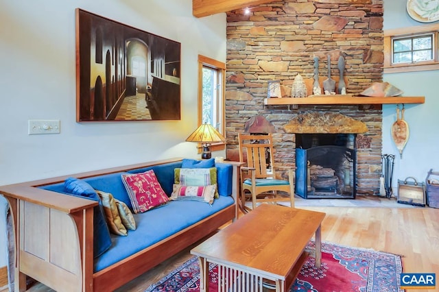 living room featuring a stone fireplace, wood finished floors, and beam ceiling