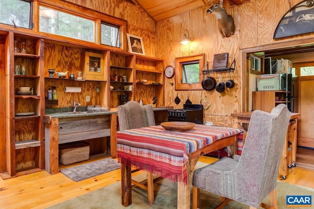 dining area featuring vaulted ceiling, wooden walls, and wood finished floors