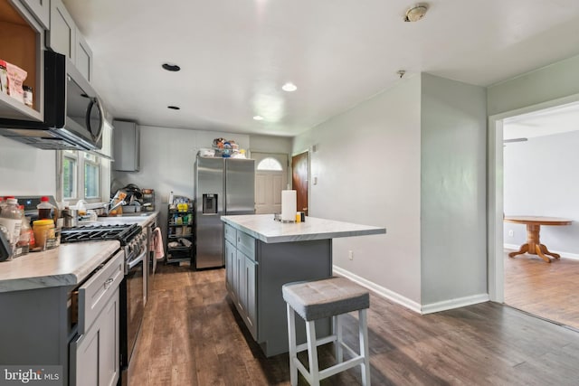 kitchen with dark hardwood / wood-style floors, gray cabinets, a kitchen island, and appliances with stainless steel finishes