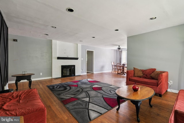 living room featuring a fireplace, ceiling fan, and dark wood-type flooring