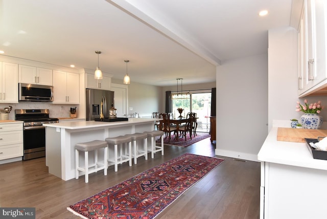 kitchen featuring a center island, dark wood-type flooring, white cabinets, appliances with stainless steel finishes, and a kitchen bar