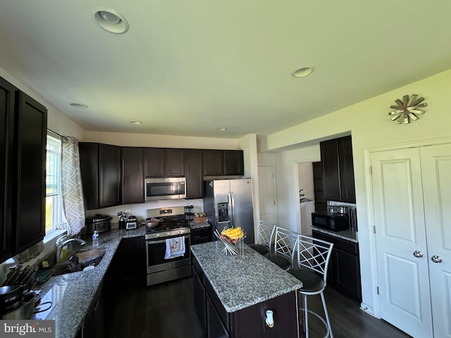 kitchen featuring light stone countertops, appliances with stainless steel finishes, a kitchen bar, sink, and a kitchen island