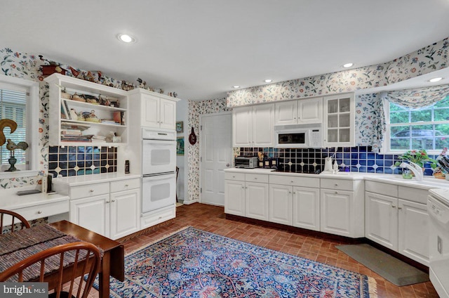 kitchen with tasteful backsplash, white cabinetry, sink, and white appliances