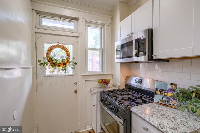 kitchen with backsplash, light stone counters, stainless steel appliances, crown molding, and white cabinetry