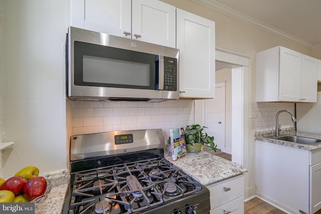 kitchen featuring sink, stainless steel appliances, light stone counters, white cabinets, and ornamental molding