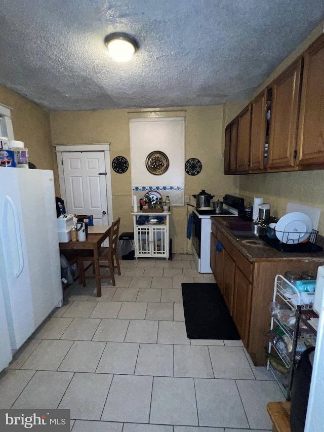 kitchen featuring a textured ceiling, white appliances, and light tile patterned floors