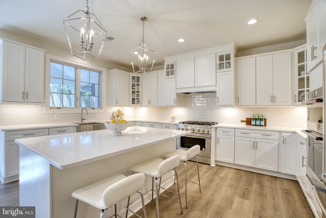 kitchen with light wood-type flooring, high end stainless steel range oven, sink, a center island, and white cabinetry