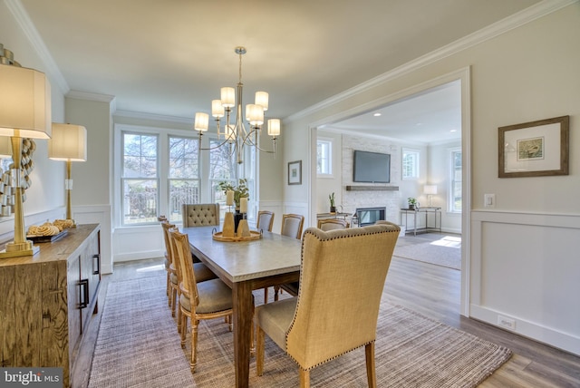 dining area featuring a brick fireplace, crown molding, a chandelier, and hardwood / wood-style flooring