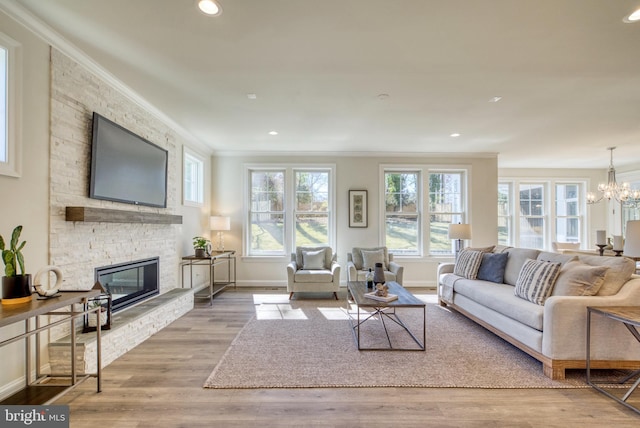 living room featuring an inviting chandelier, light hardwood / wood-style floors, a stone fireplace, and crown molding