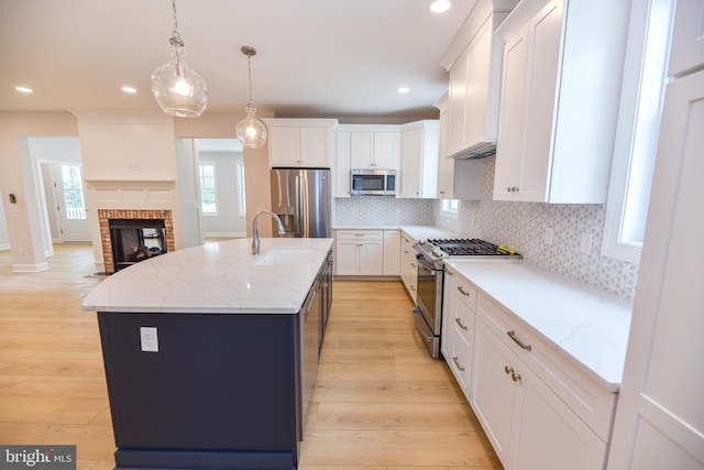 kitchen with stainless steel appliances, light stone counters, an island with sink, pendant lighting, and white cabinets