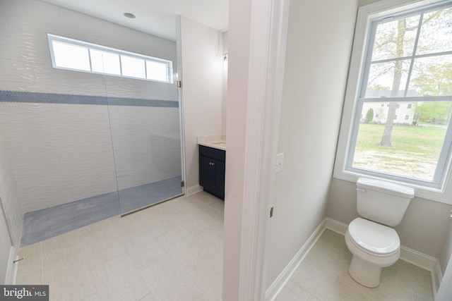 bathroom with a tile shower, vanity, toilet, and a wealth of natural light