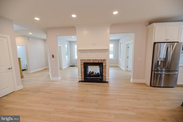 unfurnished living room featuring light wood-type flooring and a brick fireplace