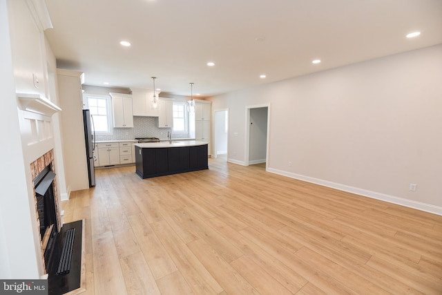 kitchen featuring white cabinets, decorative light fixtures, light wood-type flooring, and a center island with sink