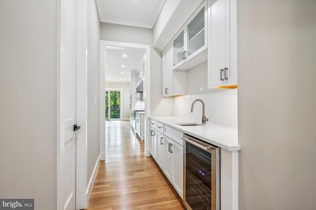 bar featuring beverage cooler, baseboards, light wood-type flooring, under cabinet range hood, and a sink