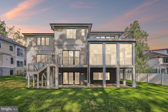 back of property at dusk with stucco siding, a fenced backyard, a lawn, and a patio