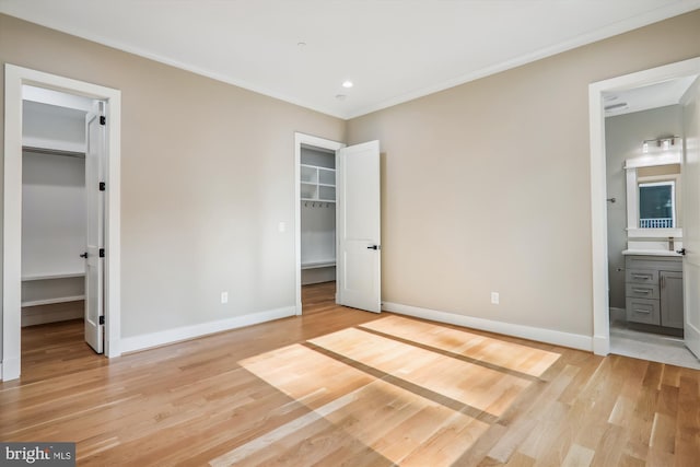 unfurnished bedroom with a spacious closet, ornamental molding, light wood-type flooring, and baseboards