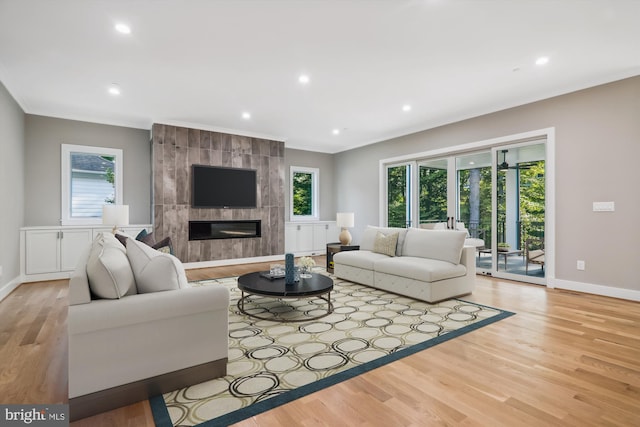 living area featuring light wood-style flooring, a tile fireplace, baseboards, and ornamental molding