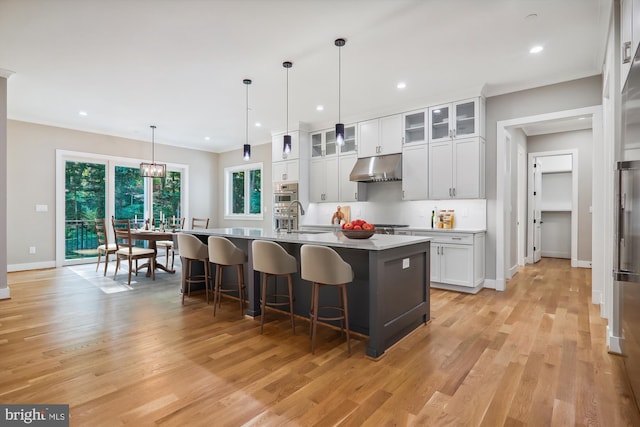 kitchen with an island with sink, ornamental molding, a breakfast bar, under cabinet range hood, and a sink