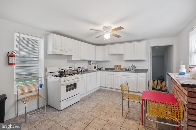 kitchen with light tile patterned floors, white cabinetry, white gas range, and ceiling fan