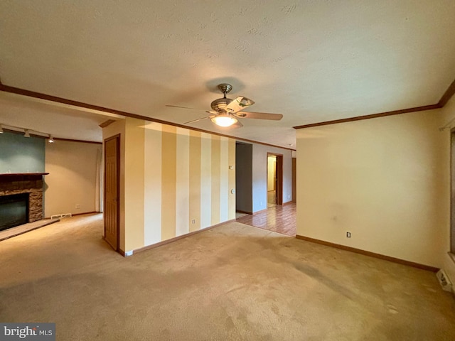 carpeted spare room with a stone fireplace, ceiling fan, a textured ceiling, and ornamental molding