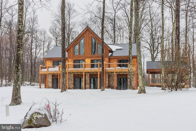 snow covered house featuring stone siding, metal roof, and a standing seam roof