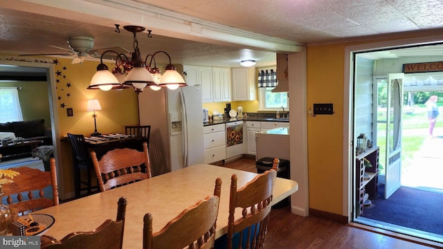 dining room with dark wood-type flooring, ceiling fan with notable chandelier, sink, ornamental molding, and a textured ceiling