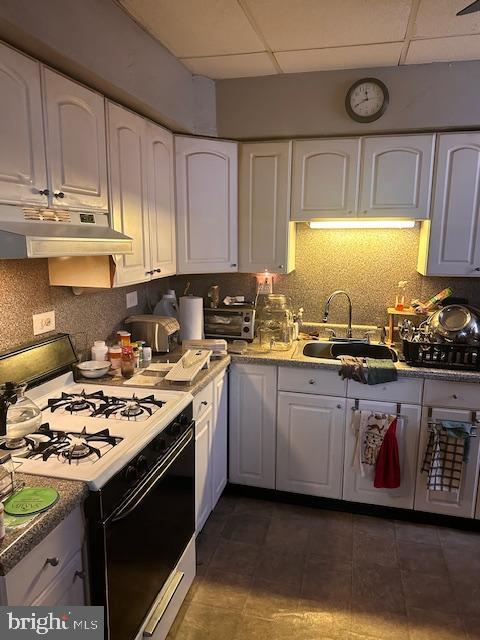 kitchen with white range with gas cooktop, a paneled ceiling, and white cabinets