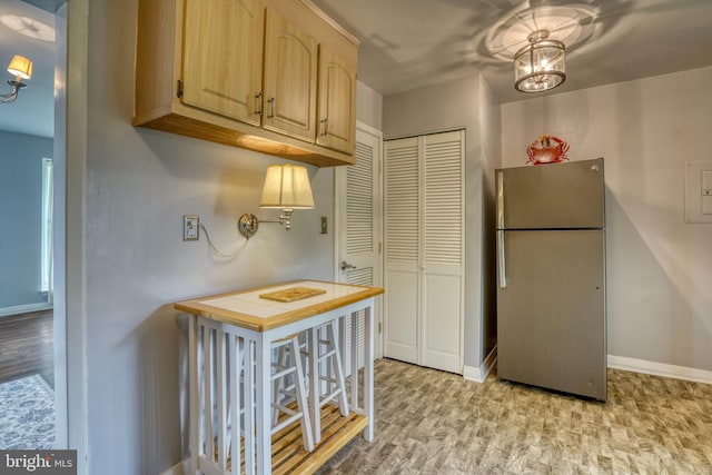 kitchen featuring light hardwood / wood-style flooring, light brown cabinetry, a notable chandelier, a breakfast bar area, and stainless steel refrigerator