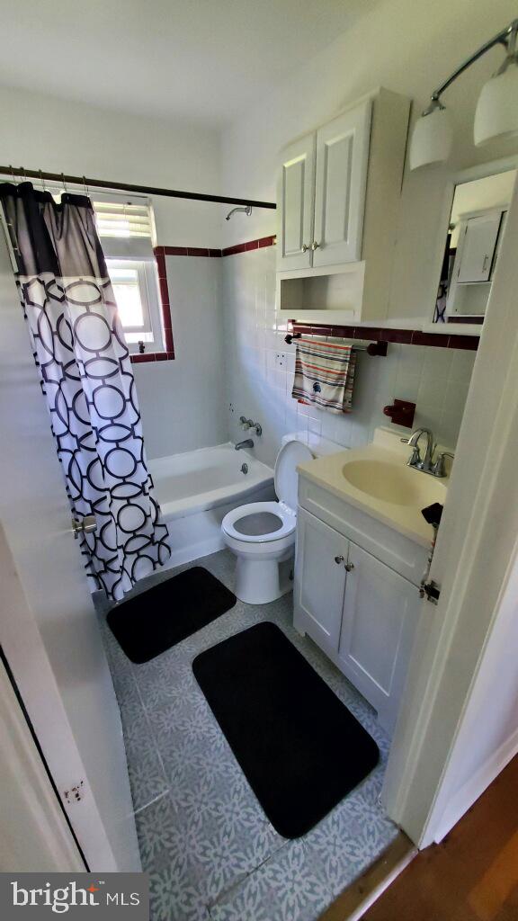 full bathroom featuring tile patterned floors, vanity, shower / bath combo with shower curtain, tile walls, and toilet