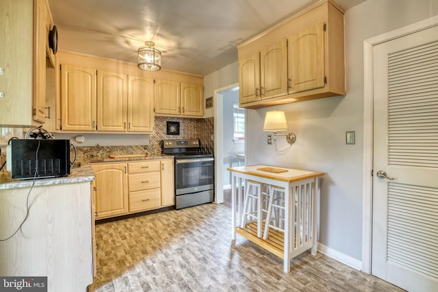 kitchen with decorative backsplash, light brown cabinetry, light wood-type flooring, an inviting chandelier, and stainless steel range with electric cooktop