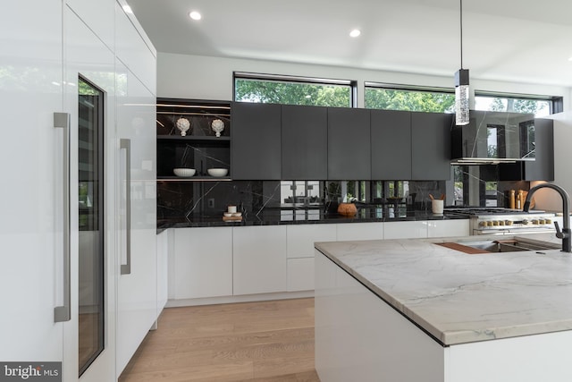 kitchen featuring decorative backsplash, light hardwood / wood-style floors, dark stone countertops, and hanging light fixtures