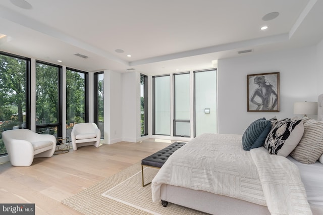 bedroom with a raised ceiling, floor to ceiling windows, and light hardwood / wood-style flooring