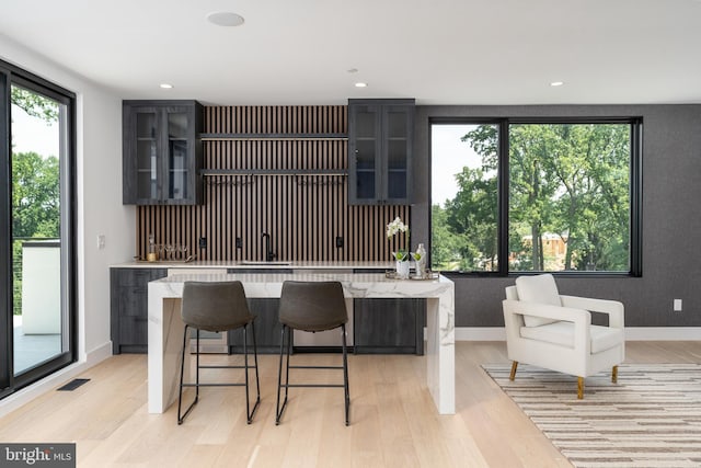 kitchen with a wealth of natural light, a center island, light stone counters, light hardwood / wood-style flooring, and a breakfast bar