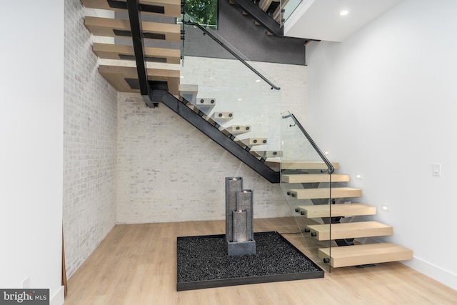 staircase featuring wood-type flooring and brick wall