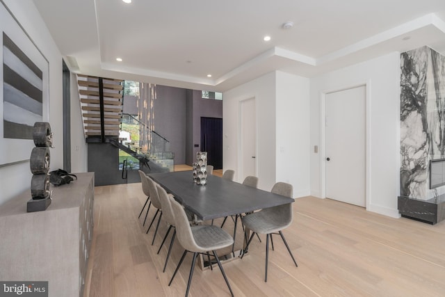 dining space with a raised ceiling and light wood-type flooring