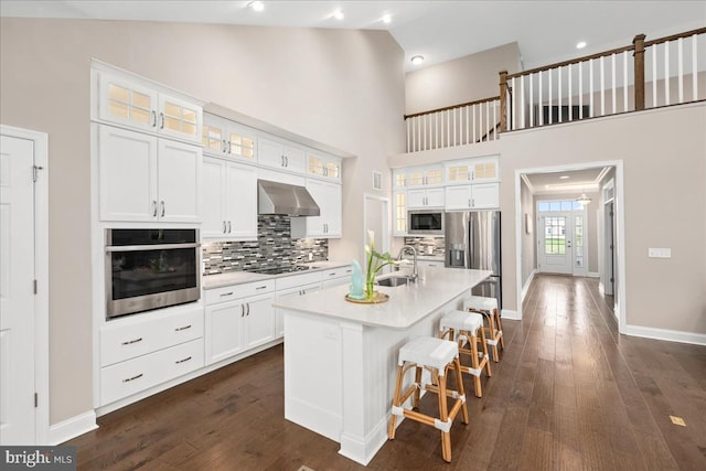 kitchen featuring appliances with stainless steel finishes, a kitchen island with sink, sink, wall chimney range hood, and white cabinetry