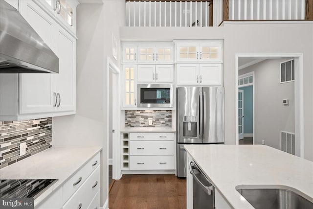 kitchen featuring white cabinetry, stainless steel appliances, light stone counters, ventilation hood, and backsplash