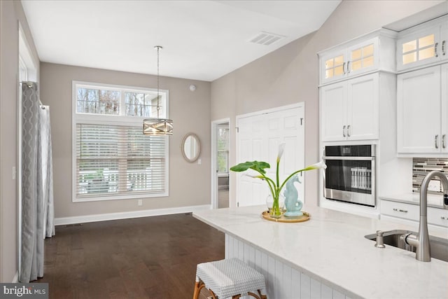 kitchen with stainless steel oven, dark hardwood / wood-style floors, pendant lighting, a breakfast bar, and white cabinets