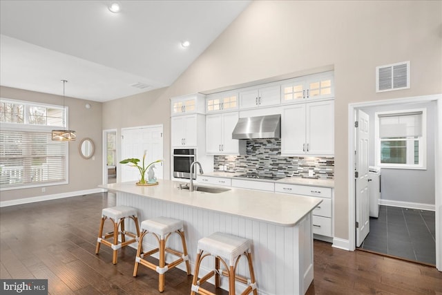 kitchen with white cabinetry, sink, wall chimney range hood, dark hardwood / wood-style flooring, and an island with sink