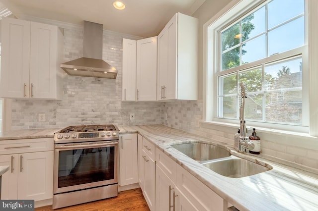 kitchen with backsplash, sink, wall chimney exhaust hood, stainless steel range oven, and white cabinetry